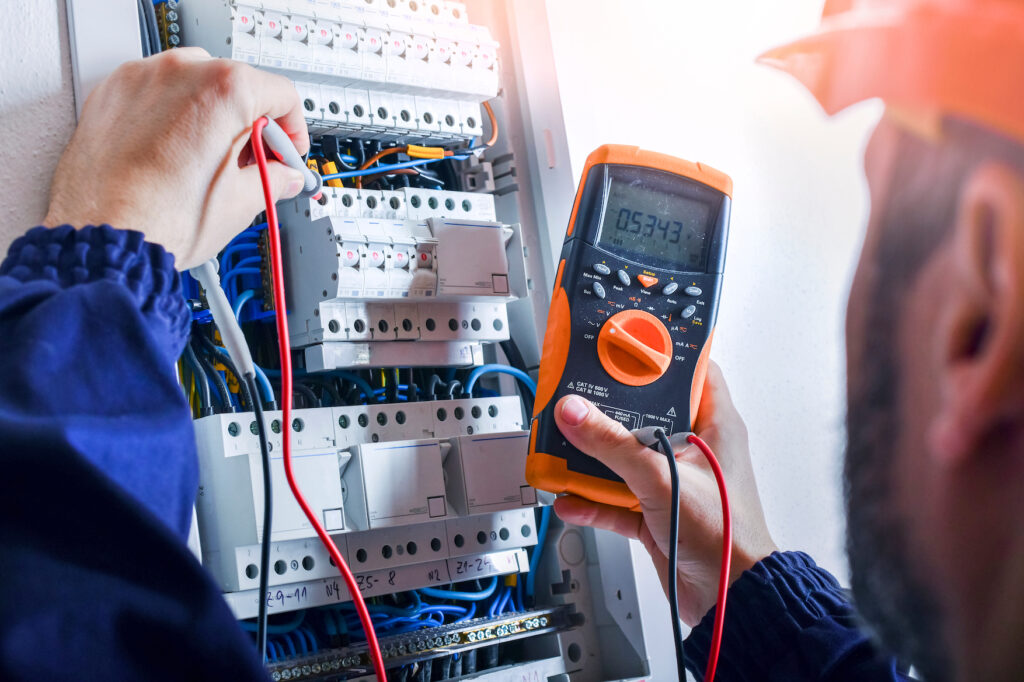 Electrician installing electric cable wires and fuse switch box. Multimeter in hands of electricians detail.